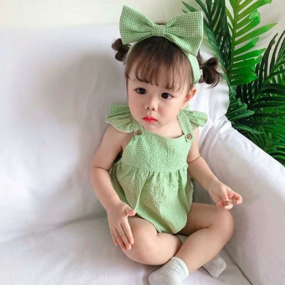 Adorable baby girl wearing a green checkered romper with a bow, available at Ju Ju Jam.