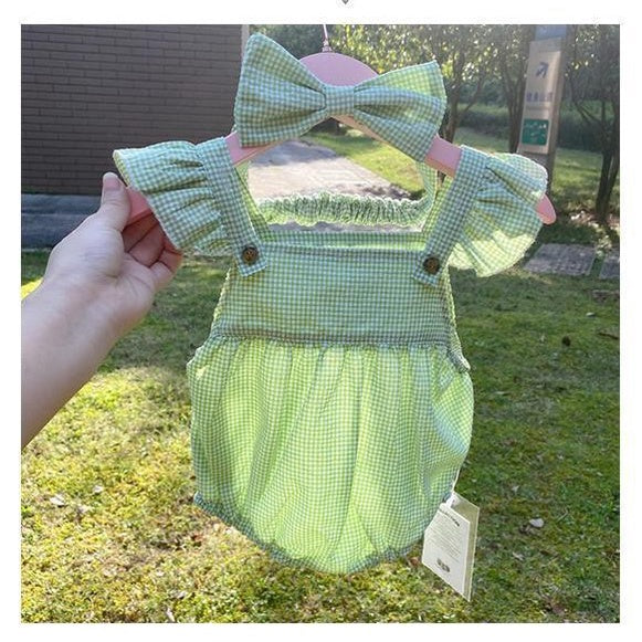 Charming baby girl in a green checkered romper with a bow accent from Ju Ju Jam.